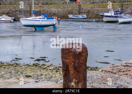 Vecchio pilastro arrugginito al porto di San Michele Monte con piccole barche e muro di pietra sullo sfondo. Cornwall, Inghilterra, Regno Unito. Foto Stock