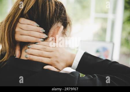 Giovane donna asiatica è seduta al lavoro e ha dolore al collo mentre è seduta in ufficio Foto Stock