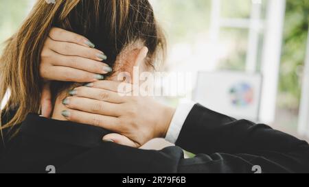 Giovane donna asiatica è seduta al lavoro e ha dolore al collo mentre è seduta in ufficio Foto Stock