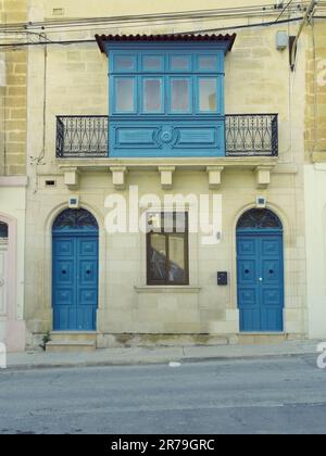 Vecchio esterno casa con due porte anteriori, una finestra e un tradizionale balcone chiuso in legno (gallarija) a Paola, Malta Foto Stock