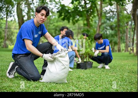 Un bel giovane e felice asiatico giovane volontario di giardinaggio maschile in un parco pubblico con la sua squadra. ecologia e sostenibilità per il concetto di comunità Foto Stock