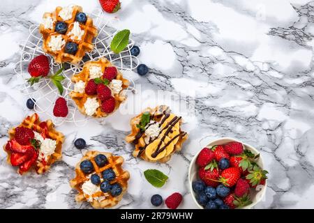 Deliziosi waffle belgi con frutti di bosco, frutta, panna montata e diversi dolcetti su marmo bianco. Vista dall'alto. Foto Stock