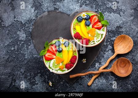 Frullato verde in ciotole per una colazione sana. Frullato biologico fresco a base di spinaci, banana, spirulina, erba di grano e lime con frutti di bosco e frutta Foto Stock