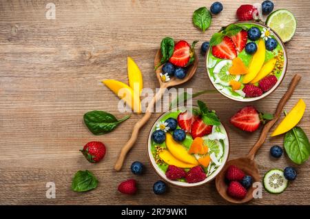 Frullato verde in ciotole per una colazione sana. Frullato biologico fresco a base di spinaci, banana, spirulina, erba di grano e lime con frutti di bosco e frutta Foto Stock