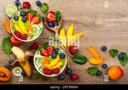 Frullato verde in ciotole per una colazione sana. Frullato biologico fresco a base di spinaci, banana, spirulina, erba di grano e lime con frutti di bosco e frutta Foto Stock