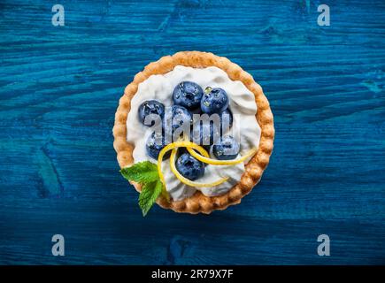 Deliziose tartine di mirtilli con crema alla vaniglia su sfondo di legno blu. Vista dall'alto. Foto Stock