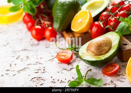 Ingredienti freschi di verdure crude per una cottura sana. Avocado, pomodori ciliegini, agrumi ed erbe fresche su tagliere di legno e tavola Foto Stock