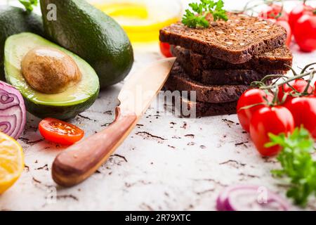 Ingredienti freschi per preparare sani panini vegetariani con pane nero, avocado e pomodori. Concetto di sana alimentazione. Foto Stock