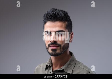 Adatta il maschio mediorientale, sorridendo sottilmente in un ritratto di primo piano. I capelli neri e la barba curati ne esaltano il fascino Foto Stock