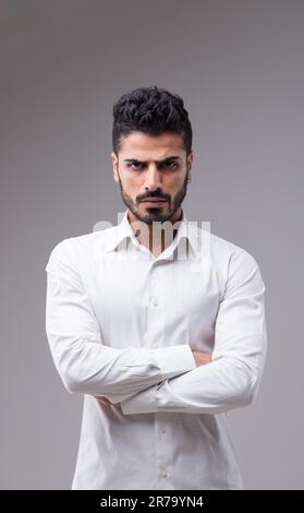 Uomo serio, quasi aggressivo in una camicia bianca. Elegante, sottile, con barba ben tenuta, capelli neri e pelle scura Foto Stock