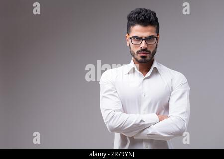 Ritratto di un uomo serio, quasi aggressivo. Bello e sottile, in una camicia bianca, le braccia incrociate. Barba curata, capelli neri, carnagione scura, colorata Foto Stock