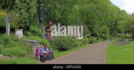 I visitatori si siedono e riposano accanto alle tombe lungo un sentiero nel cimitero di Highgate, uno storico cimitero vittoriano a nord di Londra, Inghilterra, Regno Unito Foto Stock