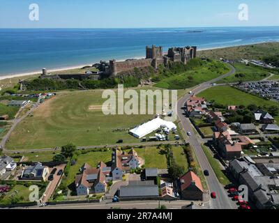 Una partita di cricket benefica si svolge sotto la goccia di ritorno del Castello di Bamburgh del Northumberland. L'Ufficio MET ha emesso una guida secondo la quale la maggior parte del Regno Unito soddisferà i criteri dell'ondata di caldo questa settimana e l'Agenzia britannica per la sicurezza sanitaria (UKHSA) ha emesso un allarme color ambra per le temperature calde. Data immagine: Mercoledì 14 giugno 2023. Foto Stock