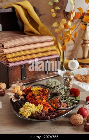 Materiale vegetale per tintura organica di tessuti su piatto, pila di tessuti tinti a mano in cassonetto di legno sullo sfondo Foto Stock