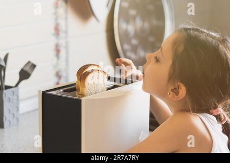 Ragazza caucasica di 5 -7 anni cucina colazione da toast in un tostapane in una cucina casa, stile di vita Foto Stock