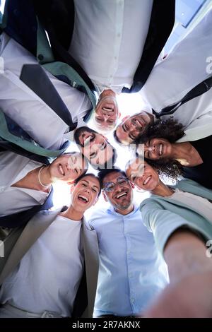 Selfie di gruppo di uomini d'affari abbracciati in cerchio, faccia in giù sorridendo e guardando la fotocamera. Foto Stock