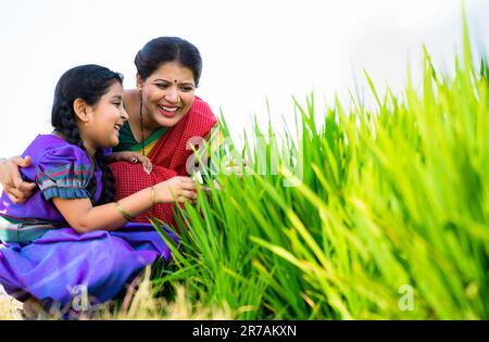 Madre indiana felice con figlia che gioca con il raccolto mentre si siede in campagna con spazio copia - concetto di maternità, stile di vita del villaggio e famiglia Foto Stock