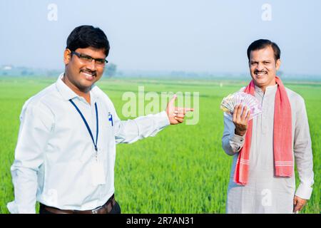 Banchiere indiano felice mostrando puntando il dito al contadino con il conteggio dei soldi a terra agricola - concetto di sostegno finanziario, bancario e agricolo. Foto Stock