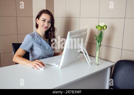 Giovane bella donna medico scrive informazioni su paziente o cliente su carta. Donna fiduciosa in uniforme infermiera siede sul posto di lavoro in medicina Foto Stock