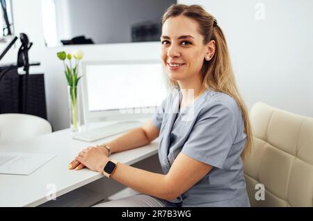 Giovane bella donna medico scrive informazioni su paziente o cliente su carta. Donna fiduciosa in uniforme infermiera siede sul posto di lavoro in medicina Foto Stock