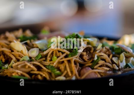 Un'allettante diffusione della cucina cinese è esposta su un piatto nero, posto su uno sfondo neutro Foto Stock