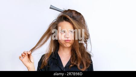 Donna triste pettinare styling aggrovigliato capelli asciutti deboli su uno sfondo bianco. Foto Stock