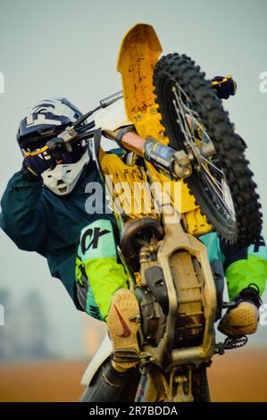 Un uomo che guida una bici sterrata attraverso un terreno polveroso, indossando un casco integrale e occhiali di protezione per la sicurezza Foto Stock