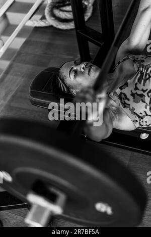 Una giovane ragazza afroamericana che lavora in una palestra, sollevando i pesi mentre fa un esercizio di pressa della panca Foto Stock