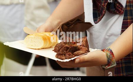 Una donna che tiene un vassoio di carta con spuntini acquistati, carne alla griglia e fette di pane francese. Foto Stock