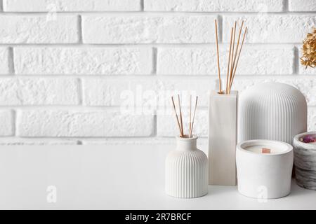 Bottiglie di diffusore a lamelle e candele sul tavolo vicino alla parete di mattoni chiari in camera Foto Stock