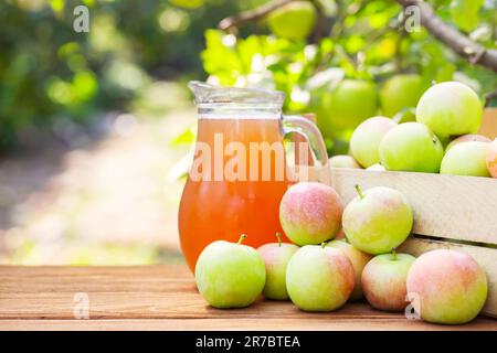 Mele, scatola di mele e brocca di succo di mela fresco su tavola di legno Foto Stock