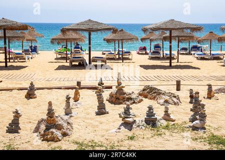 Praia de Quarteira, spiaggia e mare di Quarteira, Algarve, Portogallo, con lettini e ombrelloni e pali di pietra da meditazione Foto Stock