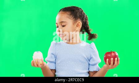 Faccia, confuso e bambino sullo schermo verde con mela, caramella e decidere in studio su sfondo mockup. Ritratto, frutta o dessert per una ragazza incerto Foto Stock