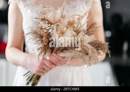 Abito da sposa bianco con pizzo sulla sposa che tiene un bouquet in stile boho. Foto Stock