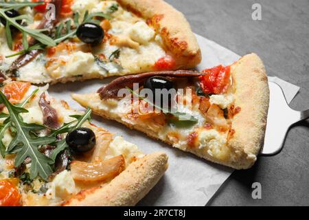 Gustosa pizza con acciughe, rucola e olive su tavola nera, primo piano Foto Stock