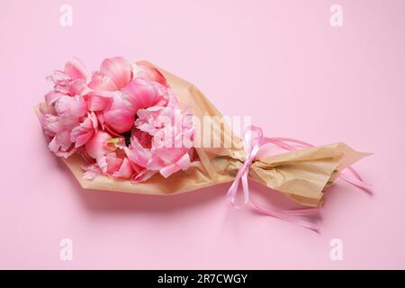 Bel bouquet di peonie avvolto in carta su sfondo rosa, vista dall'alto Foto Stock