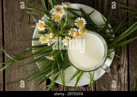 bicchiere di latte e margherite selvatiche su un tavolo al mattino Foto Stock