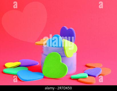 Una varietà di colorati oggetti a forma di cuore disposti in un vaso di vetro su una superficie piana Foto Stock
