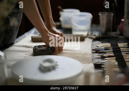 Primo piano immagine della vista posteriore di un artista maschio o di un vasaio che impastano argilla cruda sul suo tavolo di lavoro in studio. Foto Stock