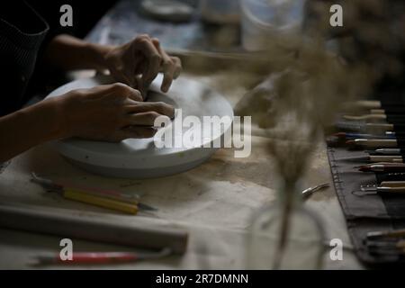 Immagine posteriore di un artista professionista maschio che fa un ornamento fatto a mano da argilla cruda in studio. Foto Stock