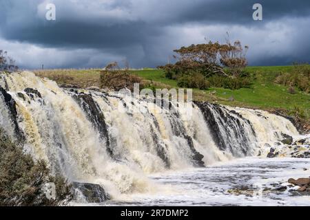 Un'ampia cascata allagata che cade nella valle sotto un cielo oscuro e tempestoso a Hopkins Falls a Warrnambool in Victoria, Australia. Foto Stock