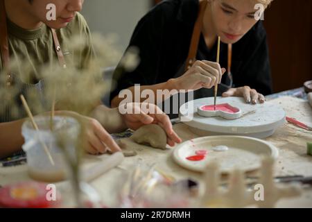 L'immagine ritagliata di un uomo si concentra sulla pittura di una lastra di ceramica in un laboratorio artigianale creativo con il suo amico. Concetto di laboratorio artigianale Foto Stock