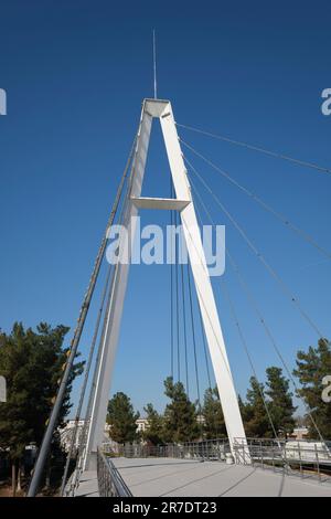 Vista del sottile, moderno, delicato, bianco sospensione, cavo soggiorno ponte pedonale su un canale. Al parco Anhor a Tashkent, Uzbekistan. Foto Stock