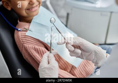 Primo piano di una dentista femmina che tiene gli strumenti mentre lavora con il bambino in clinica dentale, copia spazio Foto Stock