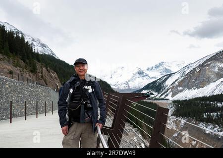 Turista sorridente e guardando la macchina fotografica al Columbia Icefield Skywalk con Sunwapta Valley dietro. Jasper National Park, Alberta, Canada. Foto Stock