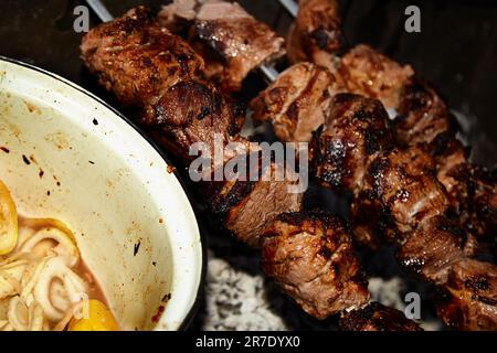 Primo piano di alcuni spiedini di carne grigliati in un barbecue.Shish kebab e tegame con cipolle e limone. Foto Stock