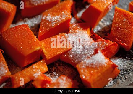 Tagliare la zucca a pezzi e cospargerla di zucchero. Focalizzazione selettiva sullo zucchero. Cottura della zucca Foto Stock