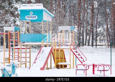 Parco giochi vuoto nel parco dopo una nevicata. Parco giochi coperto di neve con il testo polizia in ucraino. Foto Stock