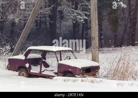 Vecchia auto abbandonata nella neve vicino alla Forest.Rusty, distrutta, auto abbandonata nella campagna dell'Ucraina in un giorno d'inverno.Vintage sfondo con un Foto Stock