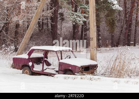 Vecchia auto abbandonata nella neve vicino alla Forest.Rusty, distrutto, auto abbandonata nella campagna dell'Ucraina in una giornata invernale. Foto Stock